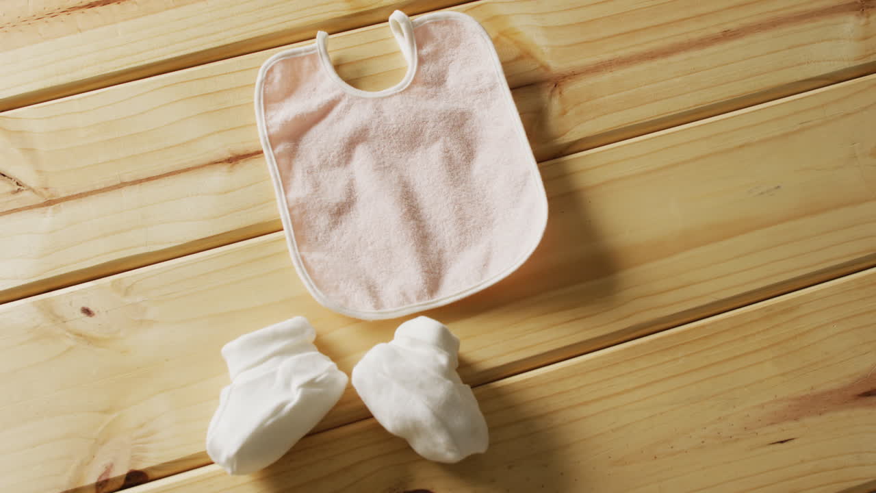 vídeo de close-up de bib bebê rosa com botas brancas em fundo de madeira