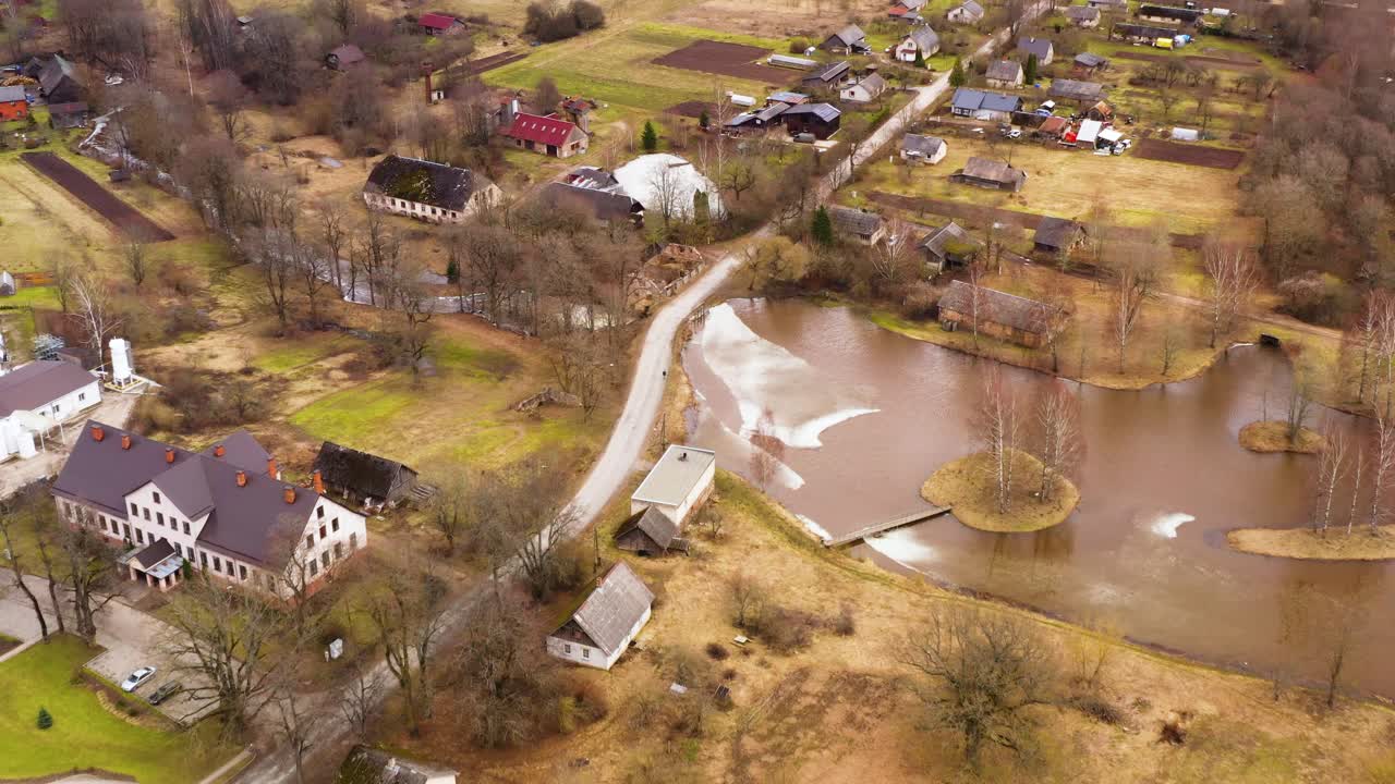 Small countryside village in spring with bare trees and flood in lake, aerial view