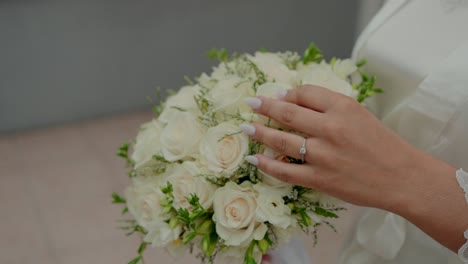 bride's hand with engagement ring gently touching a bouquet of white roses and greenery