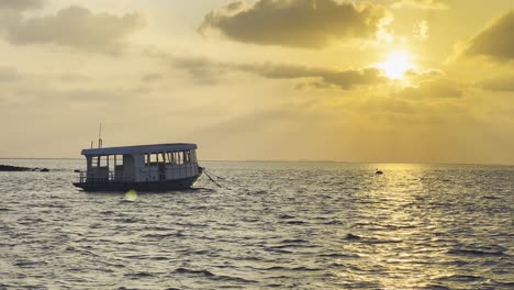 Vista-De-La-Puesta-De-Sol-En-Maldivas:-Vista-Al-Mar-Y-Quietud-Serena-Del-Horizonte-Al-Atardecer-De-La-Isla,-Con-Un-Barco-Dhoni-Tradicional-A-La-Deriva-A-Lo-Largo-Del-Horizonte,-Experiencia-De-Escapada-Tropical-Perfecta