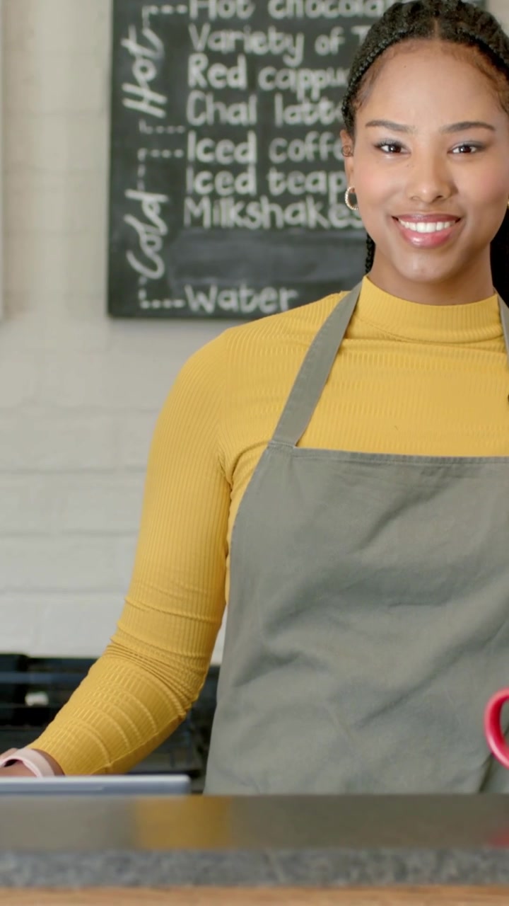 Vertical video: Opening barista in gray apron placing red mugs to serve at cafe counter, copy space