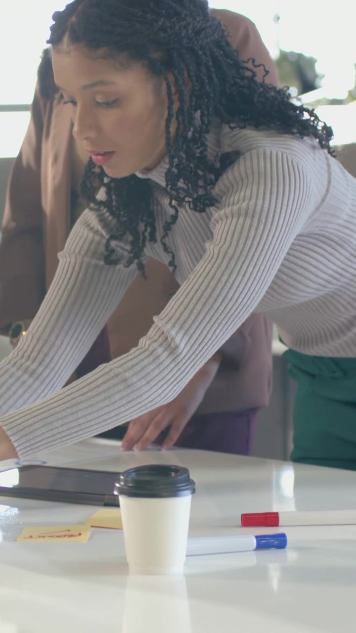 Vertical video: Leaning forward, woman in turtleneck finalizing layout on table, moving markers