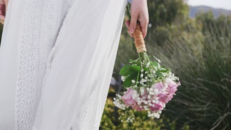 video of mid section of bride in white dress walking holding bouquet at outdoor wedding