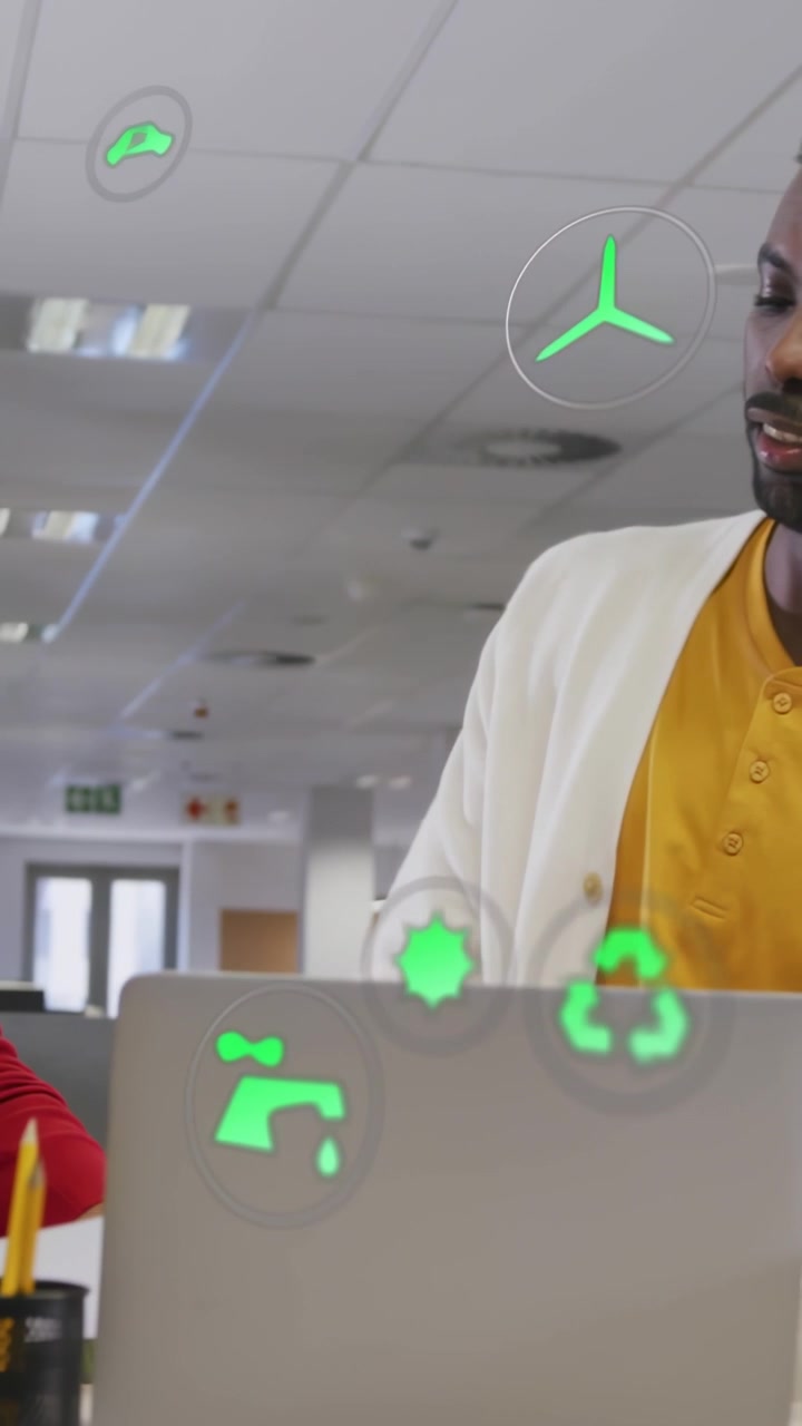 Video verticale: Un collega indica e guida un uomo in giallo che esamina un laptop, mentre icone ecologiche si allineano.