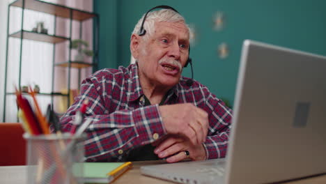 Senior man freelance wear headphone make video call talking, teaching at laptop at home office