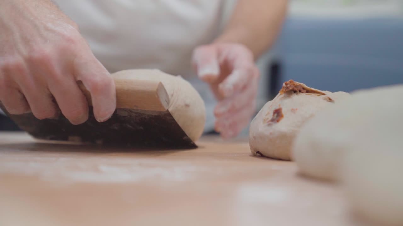 Baker preparing bread with tomato, rolling loaf with dough scraper