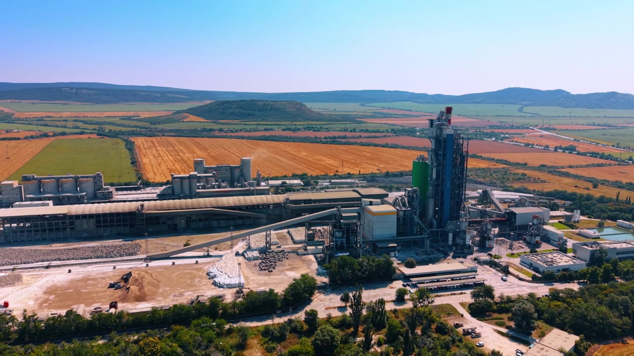 Wide aerial shot of an industrial plant with tall towers.. A manufacturing plant with towers stands among agricultural fields under a clear sky.