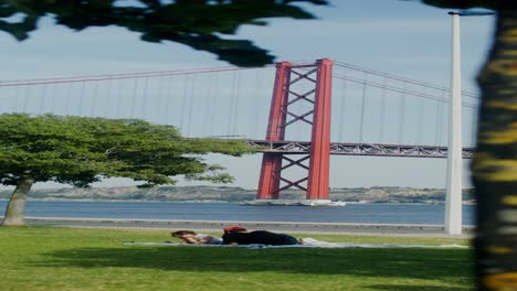 people relaxing in a park with a view of the 25 de abril bridge in lisbon