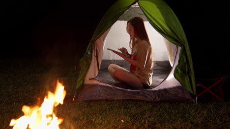 Mujer-Chica-Asiática-Charlando-Dentro-De-Su-Tienda-Acampando-Al-Aire-Libre-Por-La-Noche-Con-Fogata