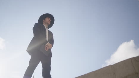 low angle shot of an orthodox man in black suit and hat walking on a sunny day