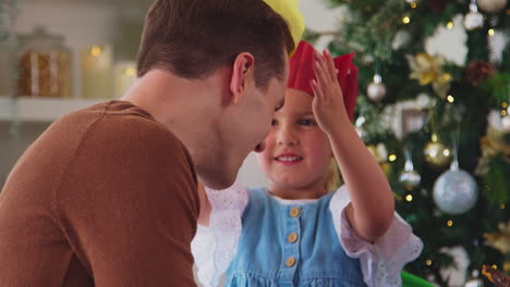 Tochter-Setzt-Vater-Einen-Papierhut-Auf,-Während-Die-Familie-Zu-Hause-Weihnachten-Mit-Essen-Feiert