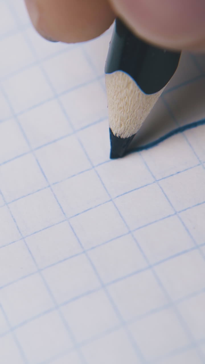 young person draws straight line with blue pencil on checkered paper sheet extreme close view
