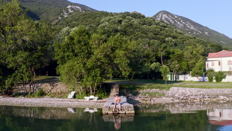 Verkleinern-Sie-Die-Aufnahme-Eines-Jungen-Mannes,-Der-Liegt-Und-Auf-Einem-Steinpier-In-Der-Bucht-Von-Kotor-In-Montenegro-Aufsteht