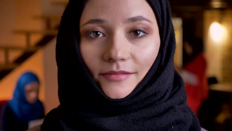 closeup portrait of young beautiful muslim female office worker in back hijab looking straight at camera with neutral facial expression