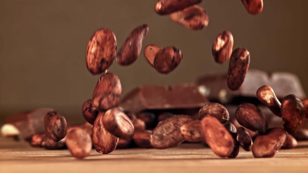 Fave di cacao che cadono su una superficie di legno con tavolette di cioccolato sullo sfondo.