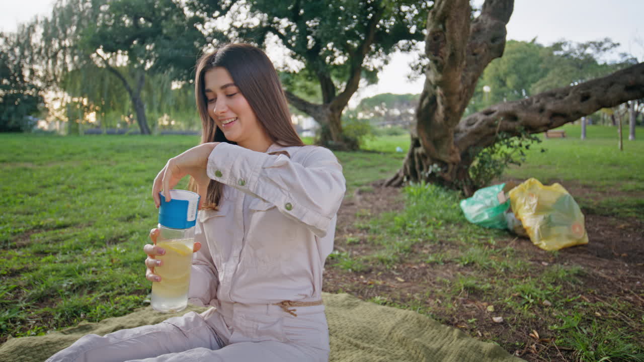 Relaxed girl enjoy hydration from glass bottle in park radiating wellness.