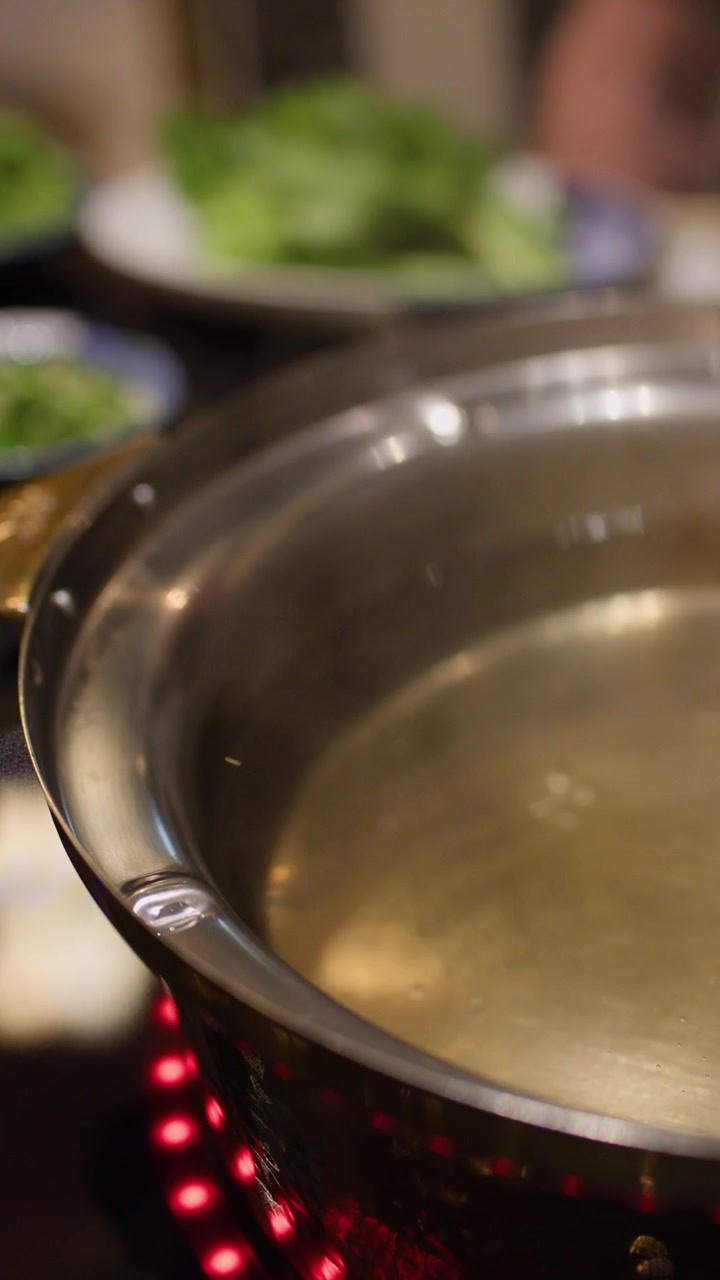 Caldo claro empieza a hervir en una olla caliente de metal, rodeado de verduras frescas e ingredientes.