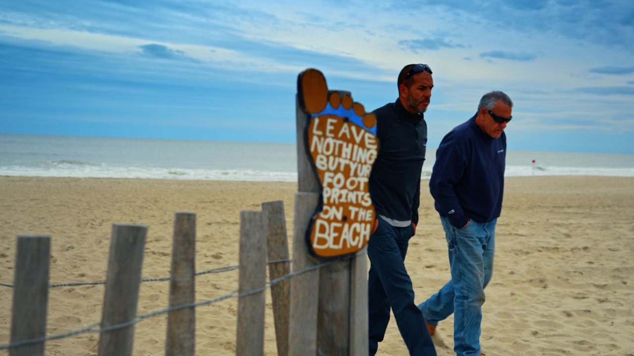 Cartello di legno a forma di piede con messaggio ecologico sulla spiaggia. Un'insegna su una staccionata di legno recita "Non lasciare altro che le tue impronte sulla spiaggia" sullo sfondo dell'oceano.