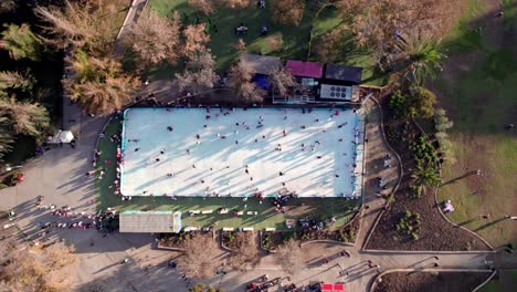 Overhead-jib-up-view-of-a-group-of-people-skating-on-an-ice-rink,-Parque-Araucano,-Santiago,-Chile