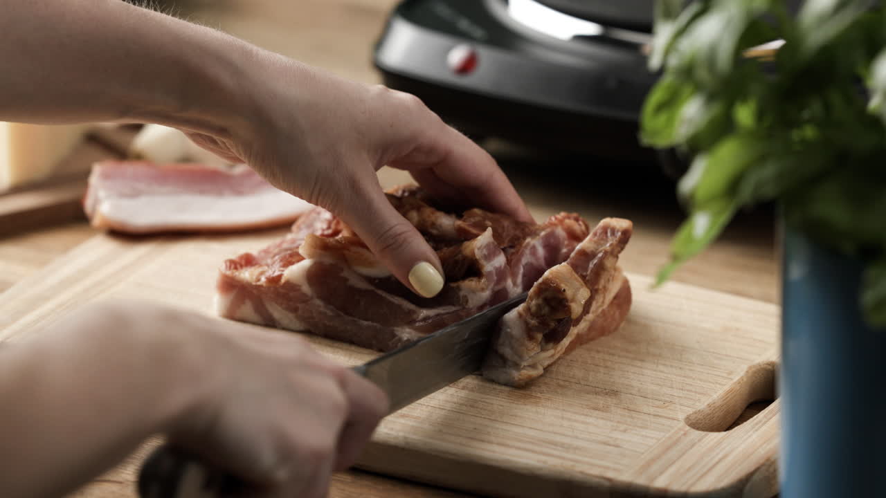 긴 칼을 사용하여 나무 도마 위에 생 훈제 삼겹살을 자릅니다.