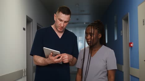 doctors and nurses discussing a patient on a tablet in a hospital corridor