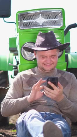 relaxed farmer enjoying his time using smartphone near his green tractor in nature a farmer is enjoying some welldeserved break time while using a smartphone next to a bright green tractor
