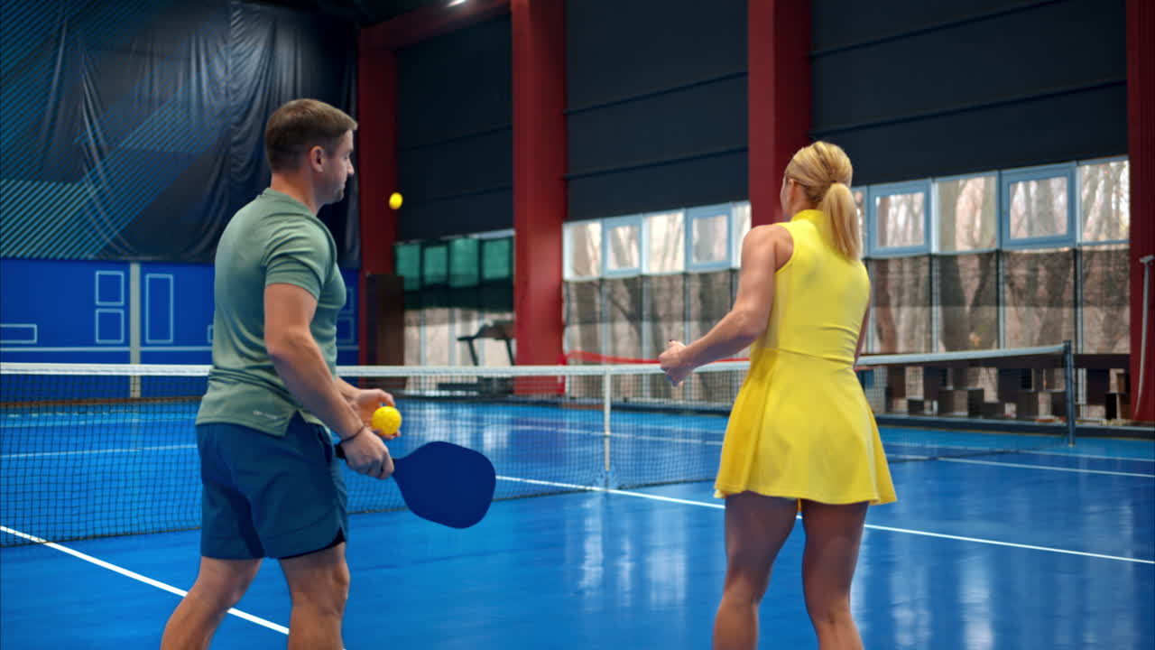 En man som lär en kvinna att spela pickleball på en inomhusbana