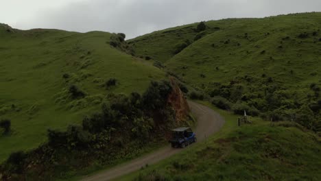 Farm-vehicle-drives-on-dirt-road-up-mountain,-elevated-terrain-ranch