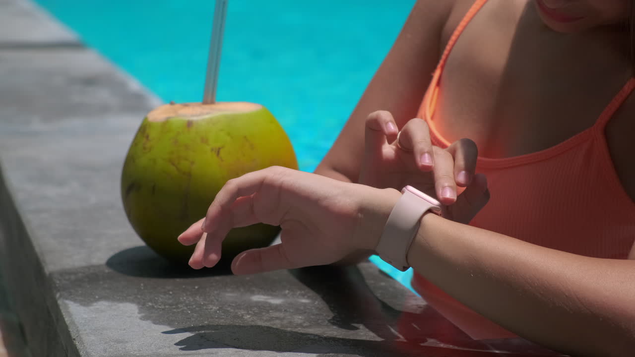 mujer relajándose en la piscina con bebida de coco y reloj inteligente