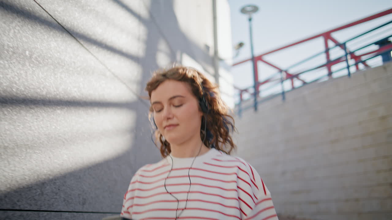 chica de moda escuchando una canción en los auriculares caminando por la calle con el jugador de cerca.