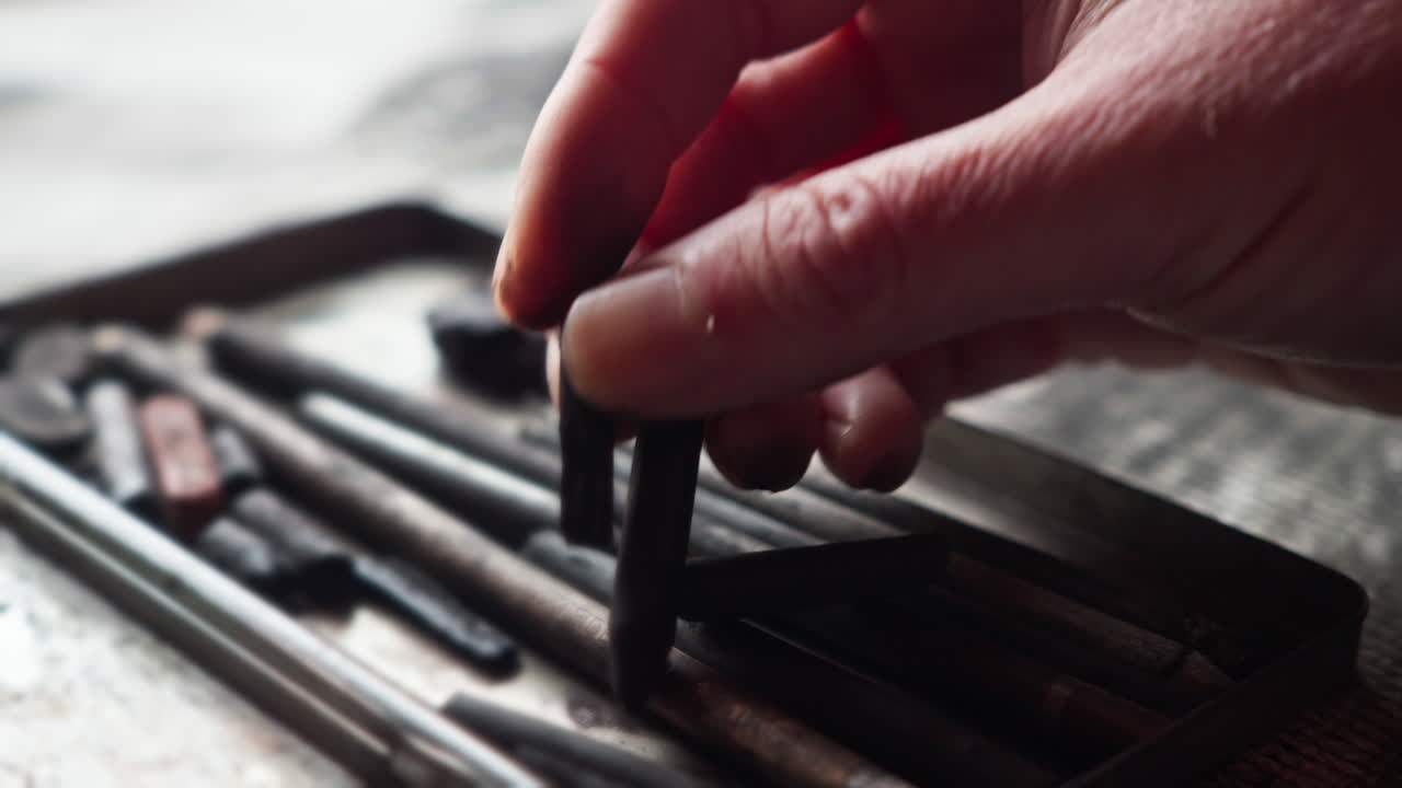 Close-up of an artist’s hand selecting the right charcoal piece, highlighting choice and precision in the creative process. Suited for storytelling around intention and craftsmanship