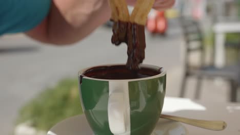 person dipping sweet churros in a hot chocolate during breakfast