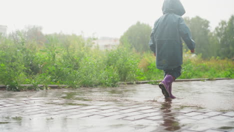 un niño con botas de lluvia camina a través de un charco