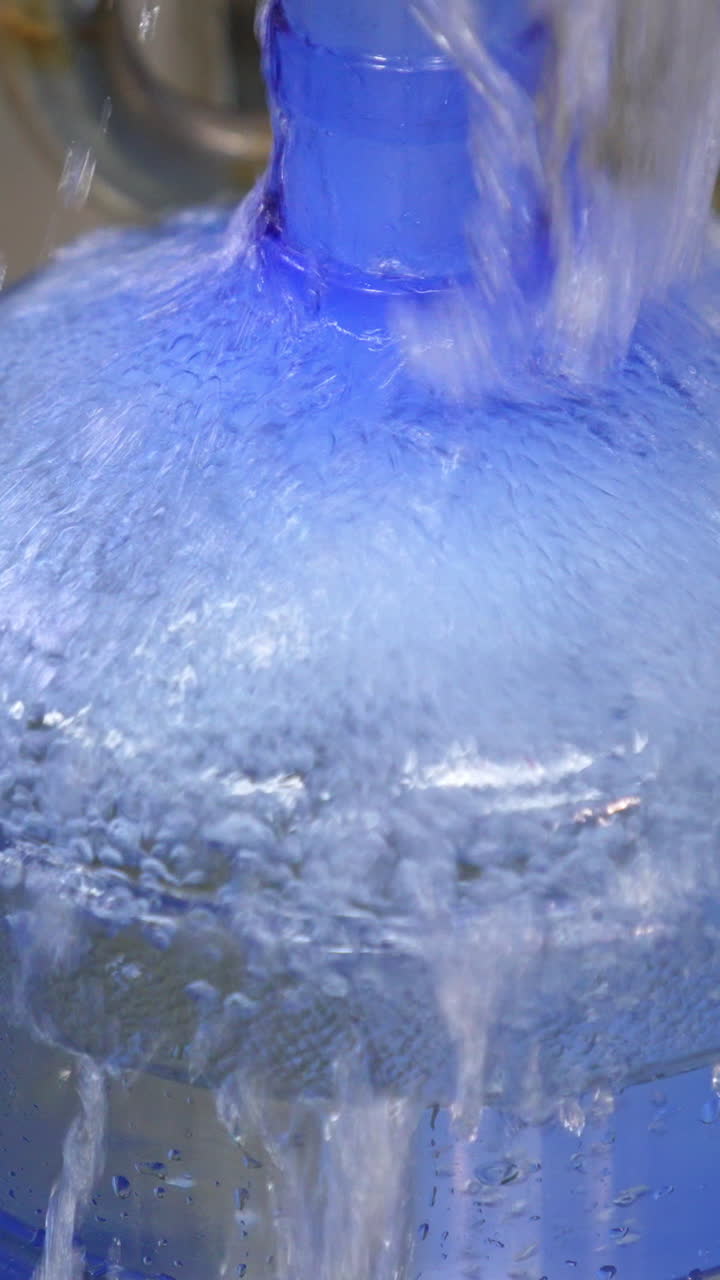 Big bottle is quickly filled with fresh water. Full bottle is moved by the conveyor line. Close up. Food factory concept. Vertical video