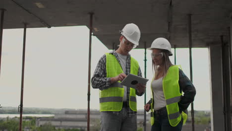 trabajador de la construcción hombre y arquitecto mujer en un casco discutir el plan de construcción de la casa hablar el uno al otro sobre el diseño sosteniendo una tableta mirar los dibujos fondo de los rayos del sol.