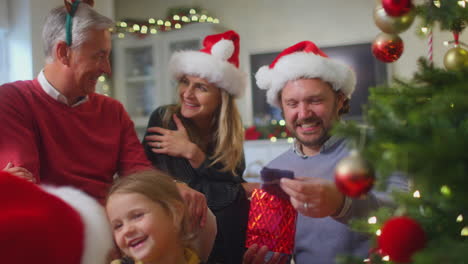 familia de varias generaciones intercambiando y abriendo regalos alrededor del árbol de navidad en casa