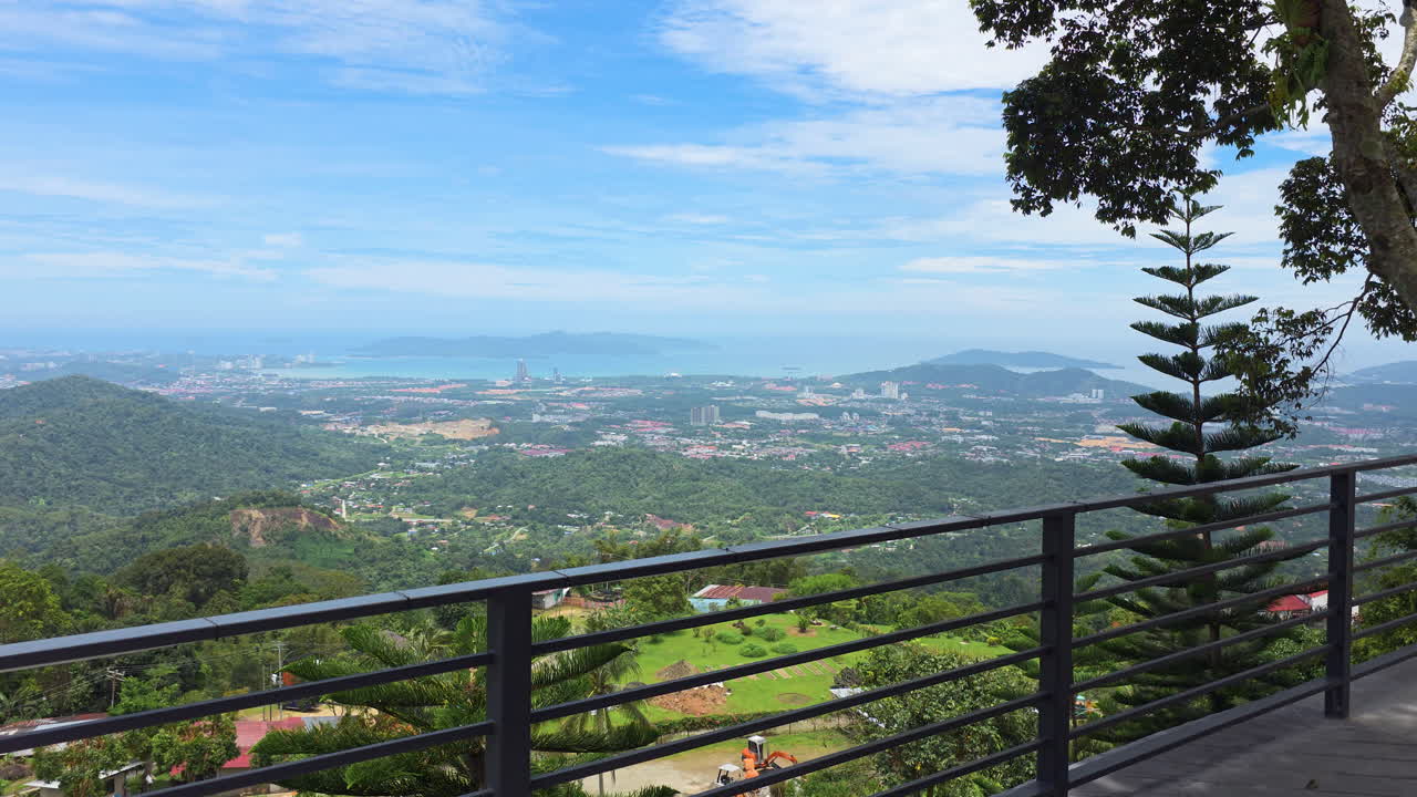 Approaching panoramic viewpoint from Kokol Hil overlooking Kota Kinabalu cityscape with lush greenery, scattered houses, and the distant coastline on sunny day