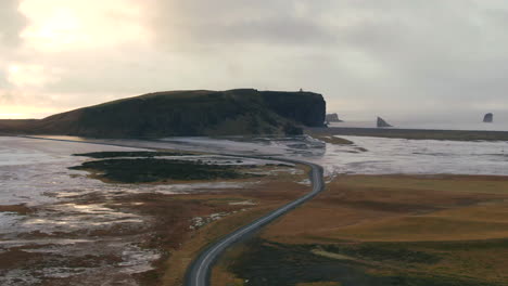 Roadway-leading-through-a-desolate-area-curving-through-two-bodies-of-water-with-a-large-hill-in-the-distance-in-Iceland
