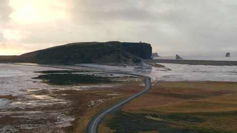 roadway leading through a desolate area curving through two bodies of water with a large hill in the distance in iceland