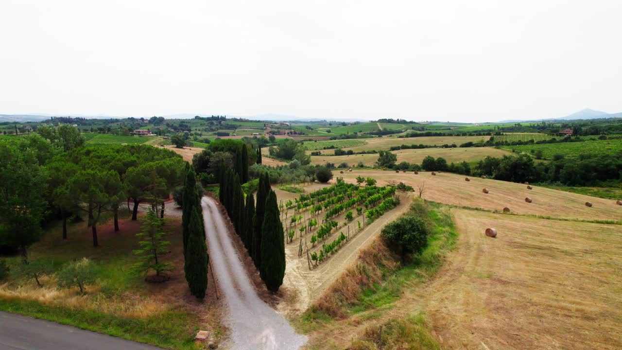 Hay Bale Roll Over Fields Near Country Road In Tuscany, Italy. Aerial Sideways Shot