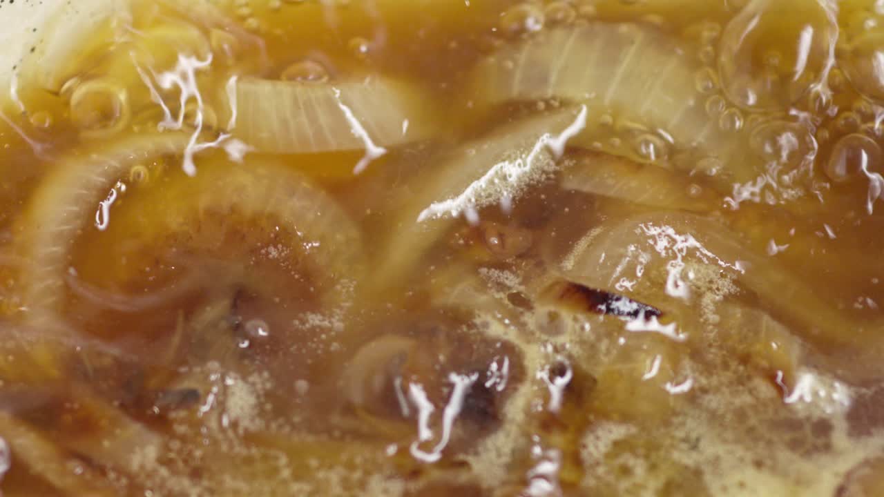 Sollevamento di una pentola che rivela una zuppa di cipolle in cottura al rallentatore. Primo piano.