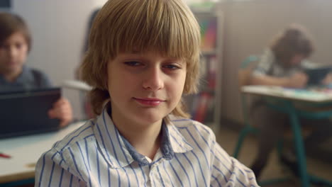 Student-sitting-at-desk-with-digital-tablet.-Cheerful-boy-posing-at-camera