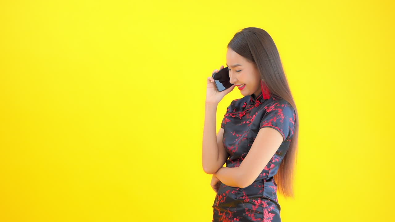 Model in black and red dress talking on cell phone and smiling. Attractive Asian woman using mobile device to talk with friend or family member. Successful businesswoman on telephone