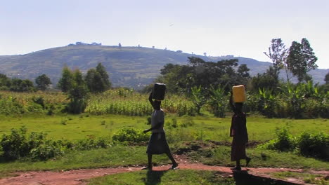 women walk along a path in a rural area carrying packages on their heads