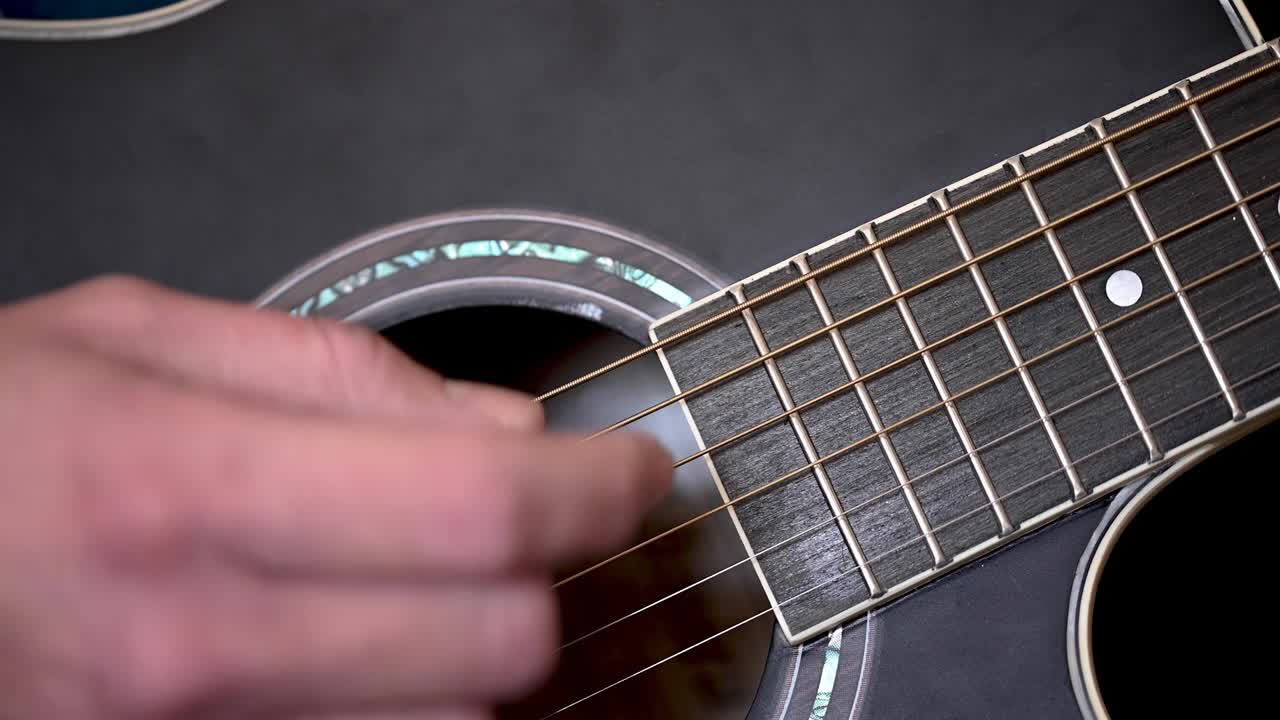 video en 4k de un primer plano de la mano de un hombre tocando las cuerdas de una guitarra acústica negra