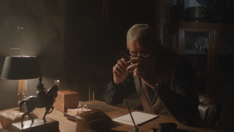 older passionate man evaluates an old silver skull watch in his office at night