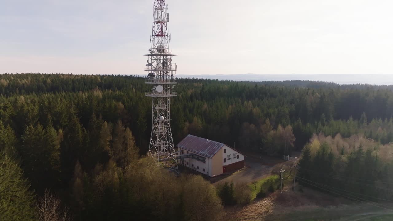A tall television tower standing in the middle of the woods. The importance of the signal for the surrounding remote villages. Drone shot.