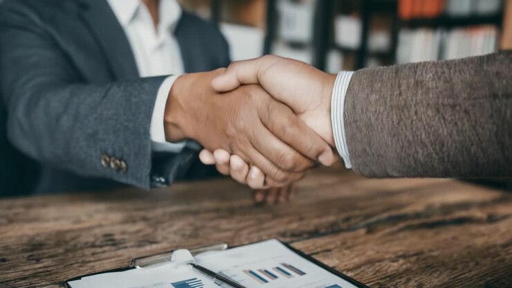 Stretta di mano professionale che simboleggia accordo e partnership tra soci d'affari in un ambiente d'ufficio con grafici e diagrammi sullo sfondo