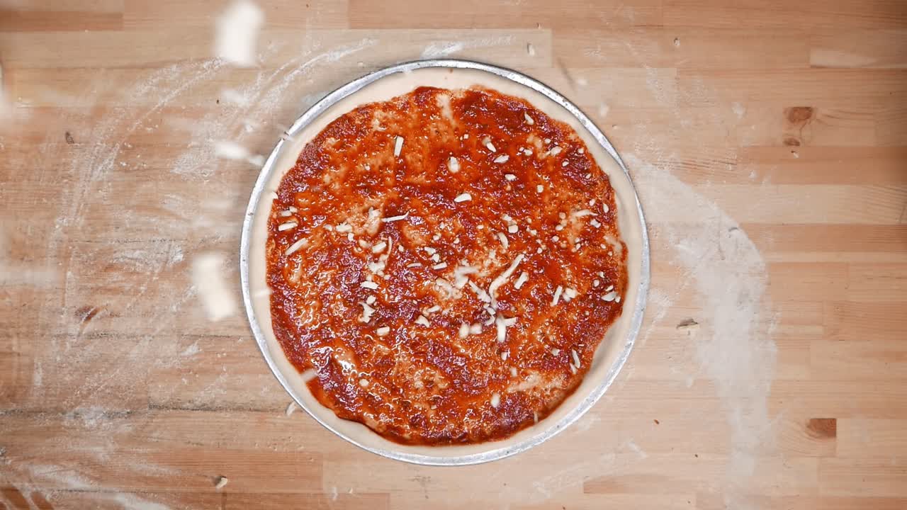 Mano dall'alto di un talentuoso chef che finisce di spolverare mozzarella su un impasto per pizza