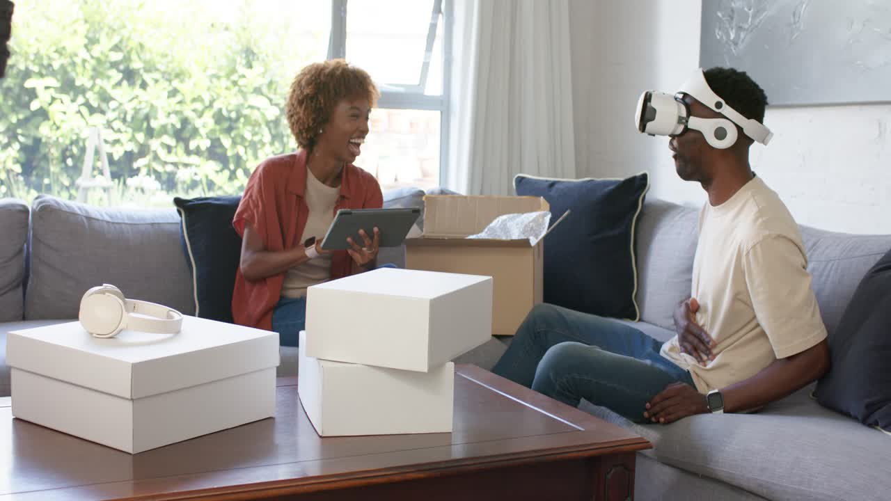 Couple at home woman unboxing tapping tablet while man wearing VR headset testing device